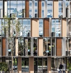 two people are walking in front of a tall building with many windows on each side