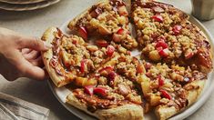 a person is taking a slice of apple crumbled pizza from a plate on a table