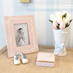 there is a vase with flowers and two baby shoes next to the picture frame on the table