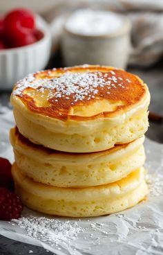 stack of pancakes with powdered sugar on top and raspberries in the background