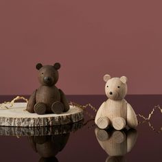 two wooden teddy bears sitting next to each other on top of a black table with a pink wall in the background