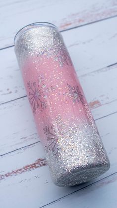 a pink and silver cup sitting on top of a white wooden table next to a bottle