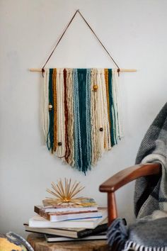 a wall hanging made out of yarn and beads with a wooden chair next to it