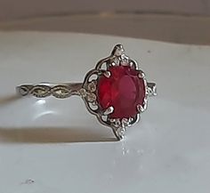 a ring with a red stone in the center on a white surface, sitting on top of a table