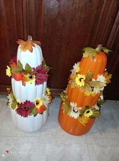 two white pumpkins decorated with flowers and leaves on the floor next to each other