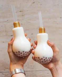 two hands holding white and gold vases with brown spots on the top, one is turned upside down