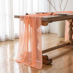 an orange table cloth draped over a wooden table in front of a window with white curtains