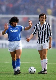 two men playing soccer on a field with fans in the stands and one holding his hand out