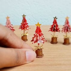 a hand is pointing at small red and gold christmas trees on a wooden table with stars