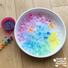 a bowl filled with lots of different colored beads next to a plastic cup on the floor