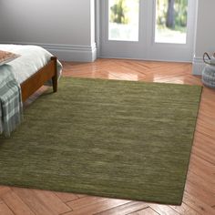 a bed room with a neatly made bed and green rugs on the wooden floor