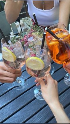 four people holding up wine glasses filled with different types of drinks and garnishes