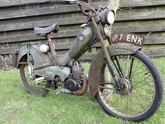 an old motorcycle parked in the grass near a wooden fence and some steps behind it