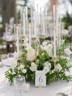 a table with candles and white flowers on it, along with place cards for the number six