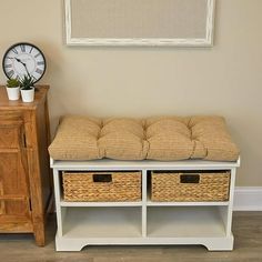 a white bench with two baskets underneath it and a clock on the wall behind it