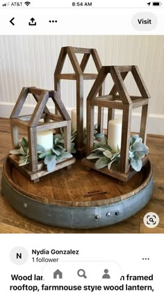 three small wooden houses with candles in them on top of a wood tray, surrounded by greenery