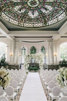 a wedding ceremony setup with white chairs and floral centerpieces on the aisle in front of a domed glass ceiling