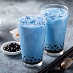 two glasses filled with blue liquid next to spoons