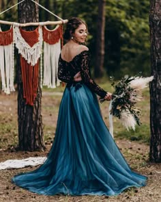 a woman standing in the woods wearing a long blue dress and holding a flower bouquet