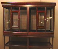 a wooden display case with glass doors and birds on the front, sitting against a wall