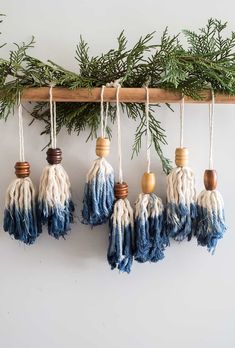 four tasselled ornaments hanging from a tree branch with pine needles and wood beads