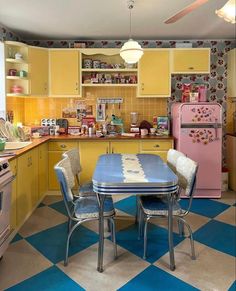 an old fashioned kitchen with yellow cabinets and checkered flooring, pink refrigerator and stove