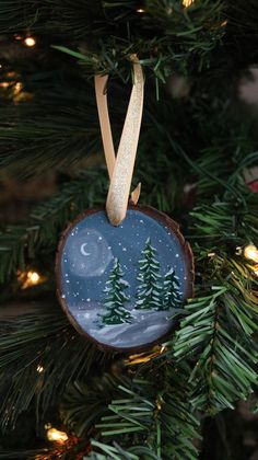 an ornament hanging from a christmas tree with the moon and trees painted on it