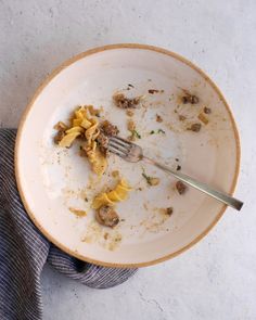 a dirty plate with food on it and a fork stuck in the bowl that is half eaten