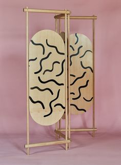 two wooden plates with black lines on them in a stand against a pink background,