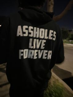 a person wearing a black hoodie with white writing on it that says asholes live forever