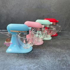 four different colored mixers sitting next to each other on a gray surface with grey wall behind them