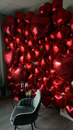 a chair sitting in front of a wall covered with red heart shaped foil balloons on display