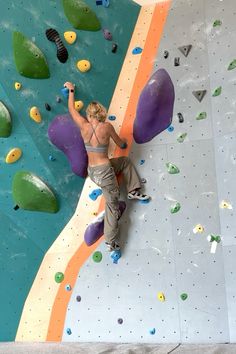 a woman climbing up the side of a wall with purple and green rock climbing equipment