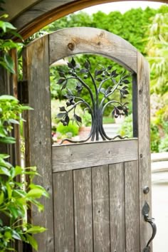 an open wooden door with a metal tree design on the top and bottom panel, surrounded by greenery