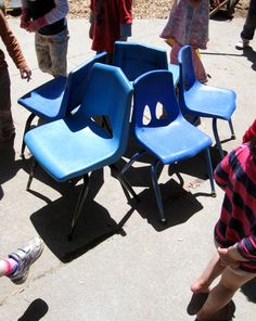 several children standing around blue chairs on the sidewalk