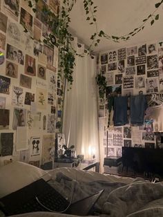 an unmade bed in a room with many pictures on the wall and plants hanging from the ceiling