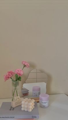 some pink flowers are in a vase on top of two books and a small mirror