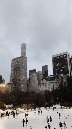 people skating on an ice rink in front of tall buildings and skyscrapers at dusk