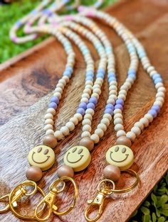 four necklaces with smiley faces on them sitting on a wooden board in the grass