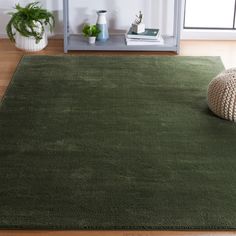 a large green rug in the middle of a room with a book shelf and potted plant