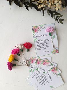 wedding stationery with colorful flowers and greenery next to it on a white surface