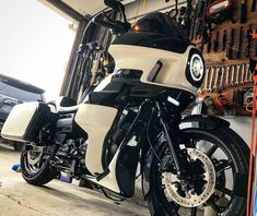 a white and black motorcycle parked in a garage next to some tools hanging on the wall