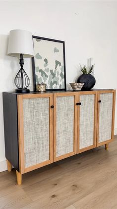 a sideboard with two baskets and a lamp on top of it in front of a white wall