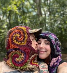 a woman wearing a crocheted hat and scarf kissing another woman's face