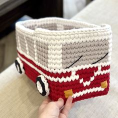 a hand is holding a crocheted basket with a red and white bus on it