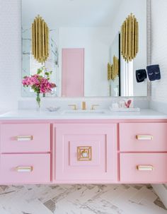 a bathroom vanity with pink drawers and gold accents on the top, along with a large mirror above it