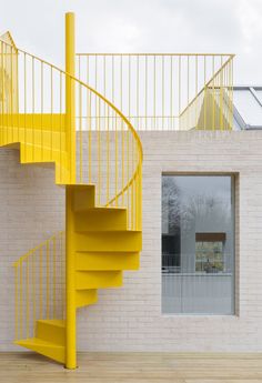 a yellow spiral staircase next to a white brick wall