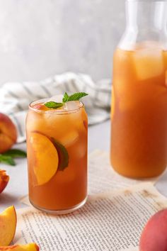 two glasses filled with peach iced tea next to sliced peaches on a table top