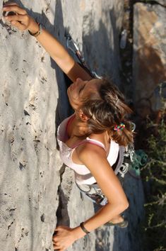 a woman climbing up the side of a mountain with her hand on top of it