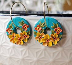 two earrings with flowers painted on them are sitting on a white surface and hanging from hooks